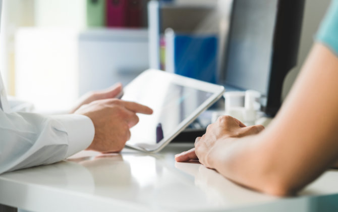 A doctor reviewing electronic health records on a tablet while talking to a patient.