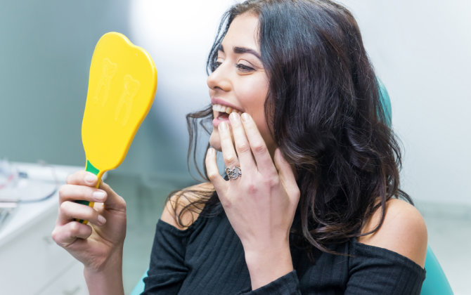 A woman is sitting in a dentist's office holding a yellow toothbrush.
